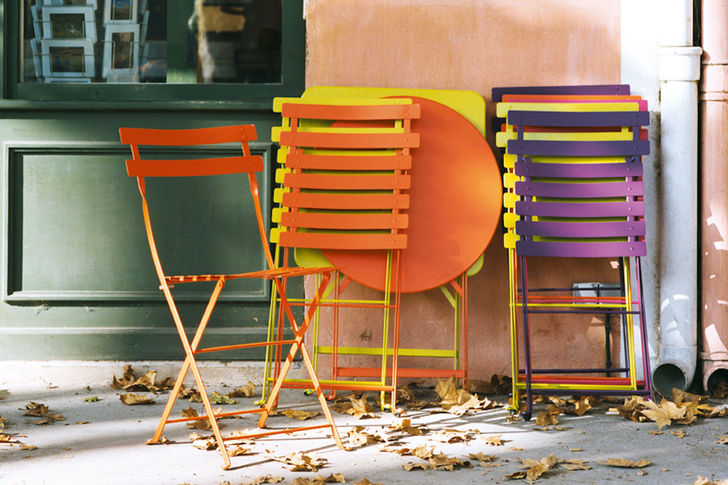Tables et chaises Fermob de différentes couleurs, pliées, et rangées contre un mur